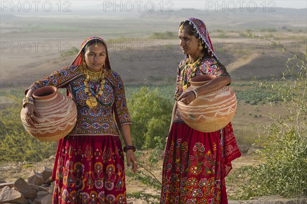 Two Ahir Women in traditional colorful clothes carrying water in a clay jug