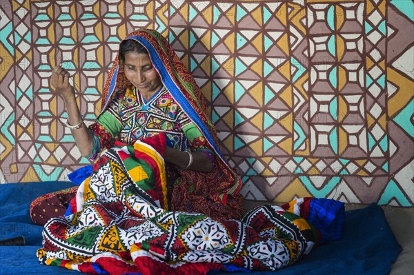 Woman in traditional clothes sewing handicraft in front of a house