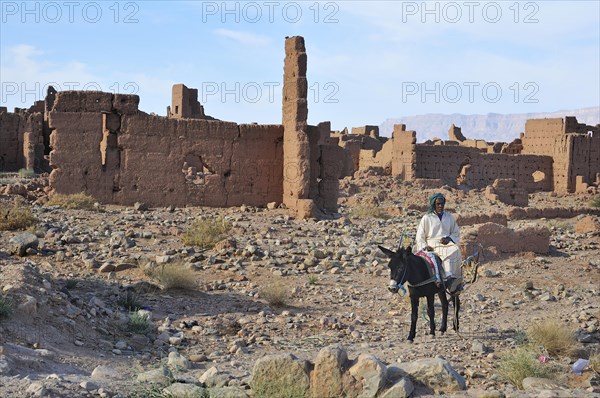 Rider on a donkey in front of dilapidated mud houses