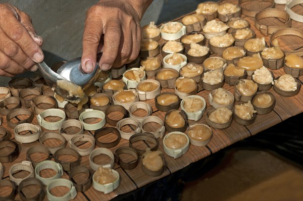 Caramelized palm sugar being filled into small moulds made of strips of palm leaves for the production of traditional palm sugar candies