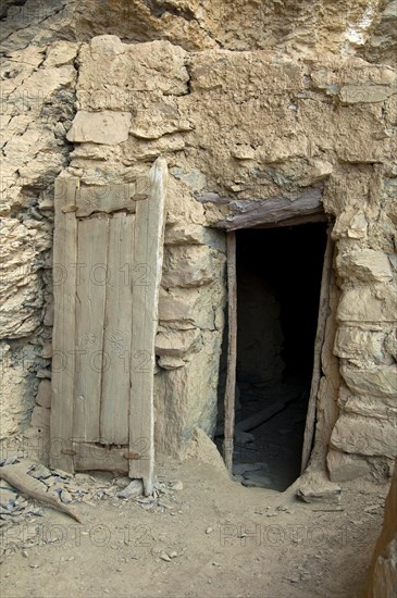 Entrance with a carved wooden door to a stone hut at the abandoned settlement of Sap Bani Khamis under a ledge in the Grand Canyon of Oman in the Wadi at Nakhar