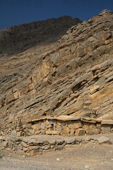 Bedouin stone house matching in colour and texture to the foot of a cliff in the mountains of Musandam