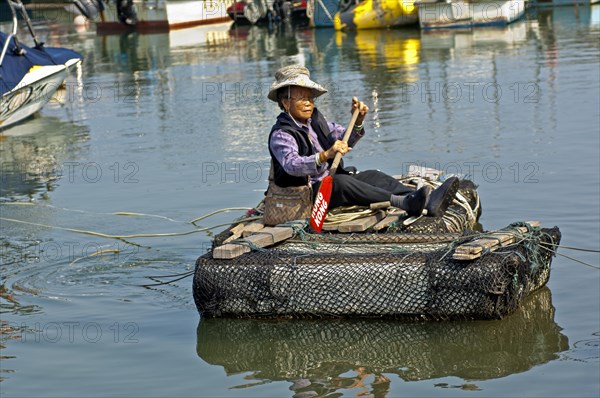 Older woman paddling over a canal in a makeshift raft