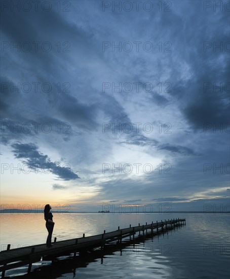 Woman standing on a wooden pier on the lake admiring the beautiful night sky