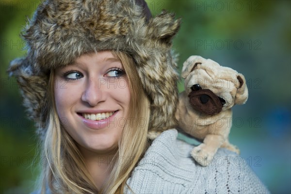 Young woman wearing a fur hat with a plush pug on her shoulder