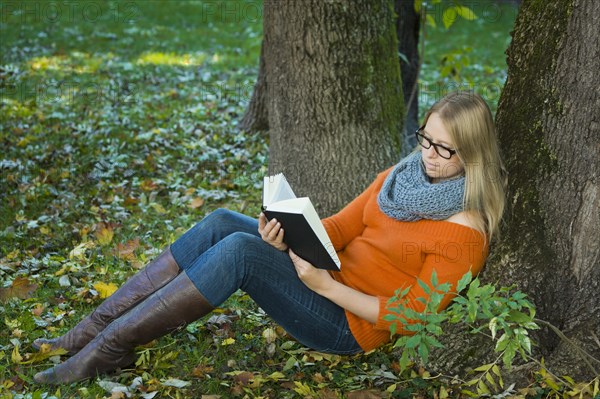 Young woman wearing glasses sitting in the park and reading a book