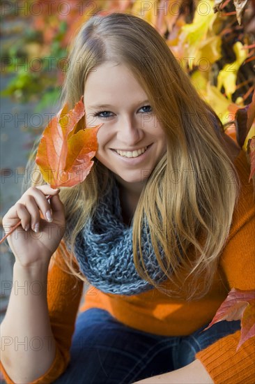 Young woman wearing a thick scarf and holding an autumnal coloured leaf in her hand