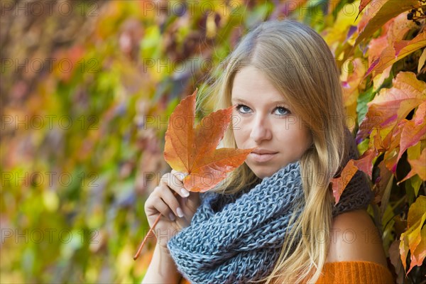 Young woman wearing a thick scarf and holding an autumnal coloured leaf in her hand