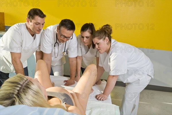 Several doctors and midwives with concerned expressions looking between the legs of a woman during childbirth