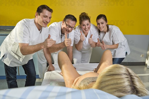 Several doctors and midwives encouraging a woman during childbirth with their thumbs up