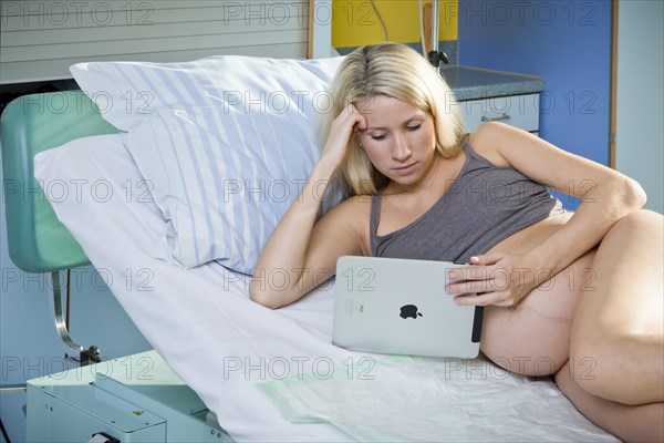 Pregnant woman lying in the delivery room on the delivery bed and looking at a tablet PC