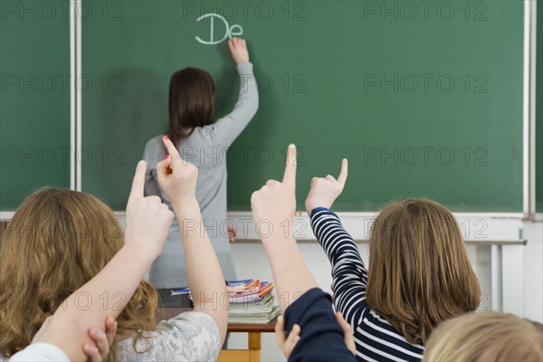 School children raising their arms to answer during class