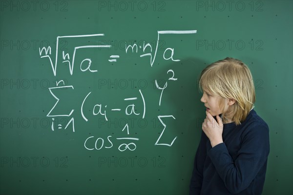 Schoolboy pondering a mathematical formula on a school blackboard