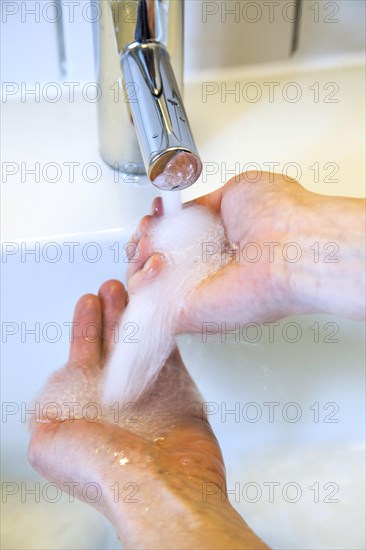 Person washing their hands under running water from a faucet