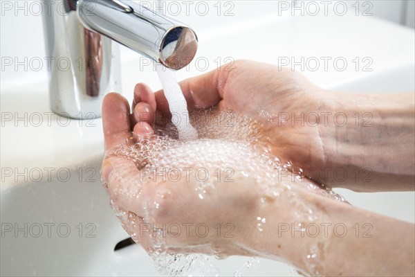 Person washing their hands under running water from a faucet