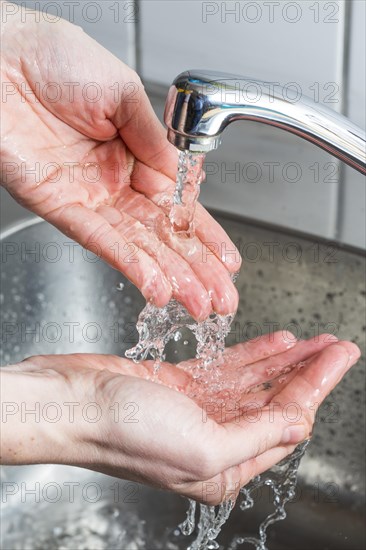 Person washing their hands under running water from a faucet