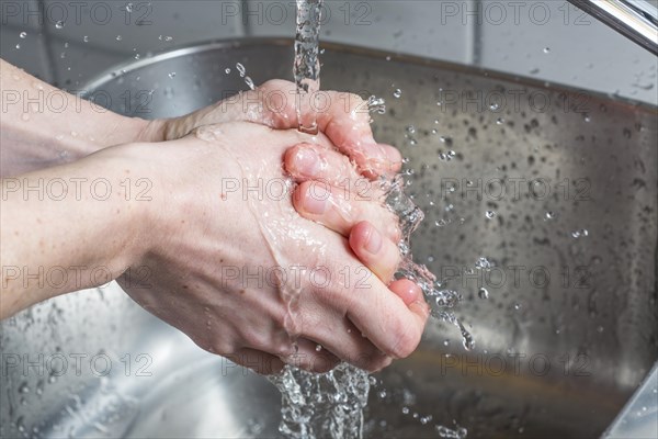 Person washing their hands under running water from a faucet