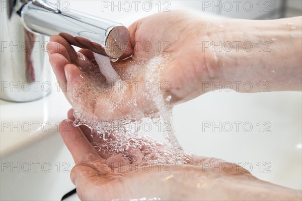 Person washing their hands under running water from a faucet