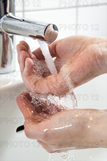 Person washing their hands under running water from a faucet