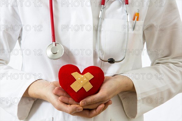 Female doctor holding a red heart with a plaster in her hands