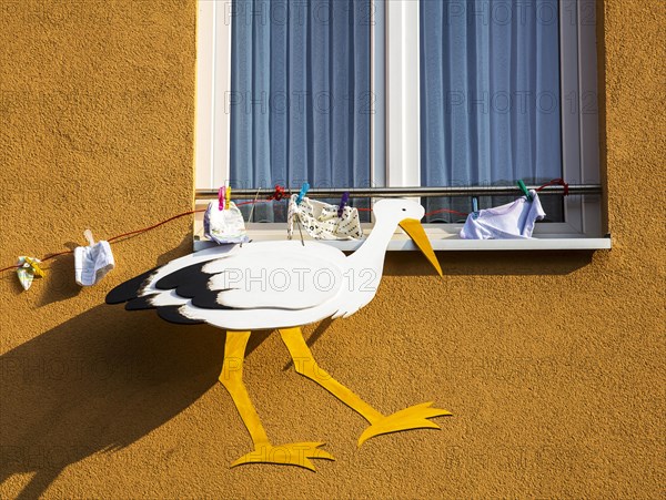 Stork figure and baby clothing attached to a house