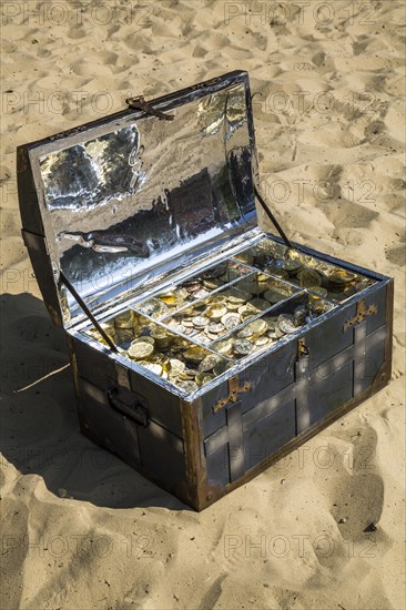 Treasure chest with gold and silver coins on the sand