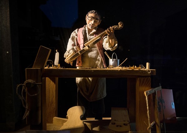 Violin maker as wooden figure at work in violin making workshop