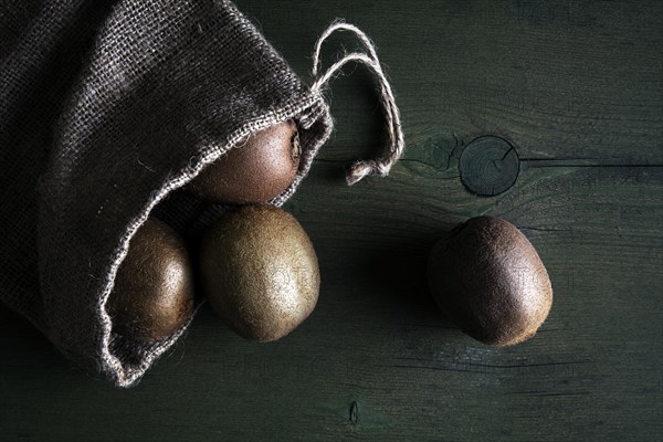 Kiwi fruits in jute sack lying on a wooden table