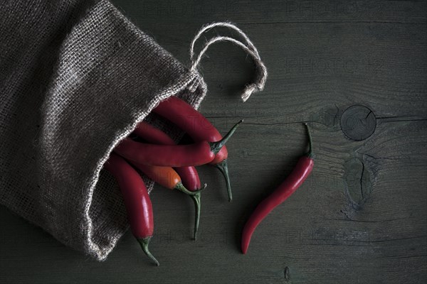 Red peppers in a jute sack lying on a wooden table