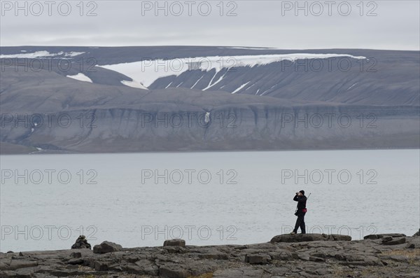 Person with a rifle over their shoulder looking around with binoculars for polar bears