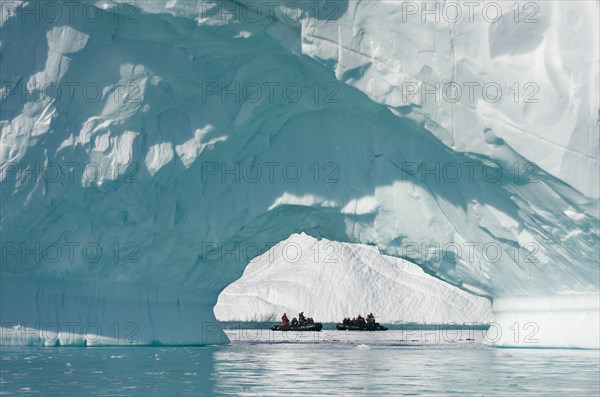 Zodiac inflatable boats seen through the arch of a large iceberg