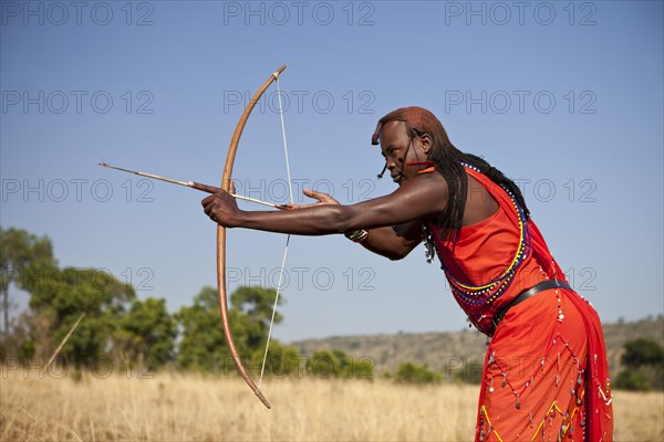 Maasai warrior wearing traditional dress while doing archery with a bow and arrow