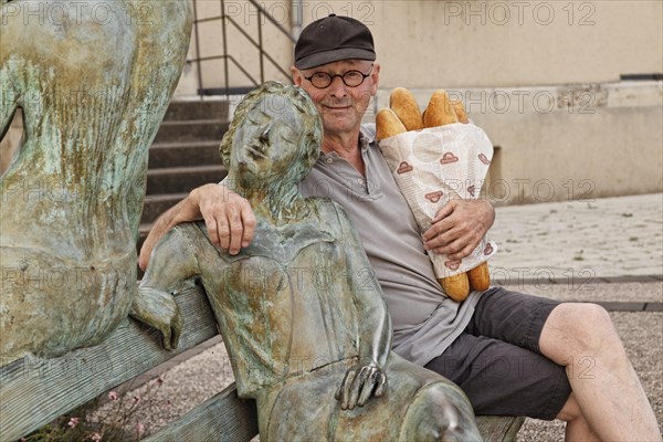 Man holding baguettes sitting beside a sculpture in front of the Town Hall