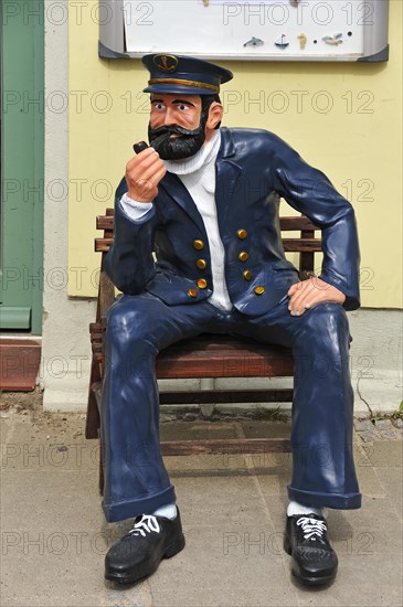 Life-size sailor figure on a bench in front of a house