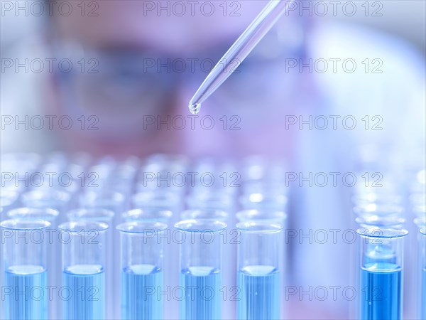 Laboratory assistant dripping liquid with a pipette into test tubes