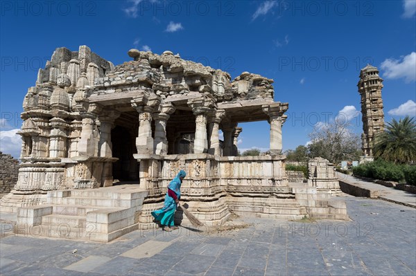 Woman sweeping the stone slabs in front of temple ruins