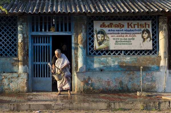 Old woman moistening the pavement in front of her house