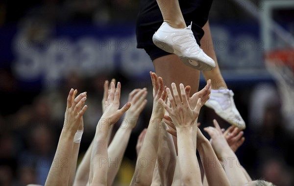 Cheerleaders stretching out their hands to support a cheerleader above