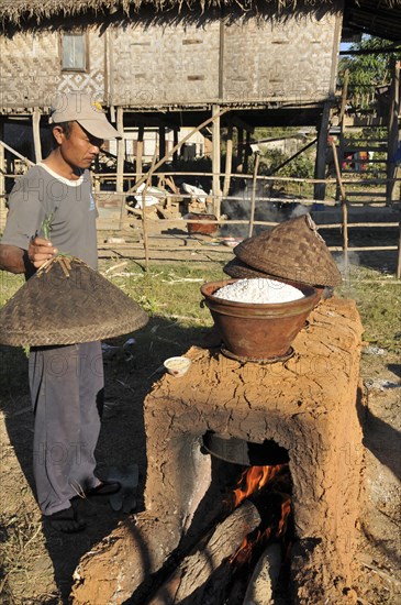 Man steaming sticky rice over an open fire for the Full Moon Festival in December