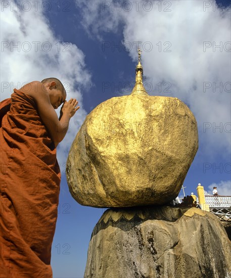 Buddhist Monk praying in front of the Golden Rock or Kyaiktiyo Pagoda