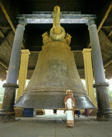 Elderly woman with a wooden mallet standing in front of the largest intact bell in the world