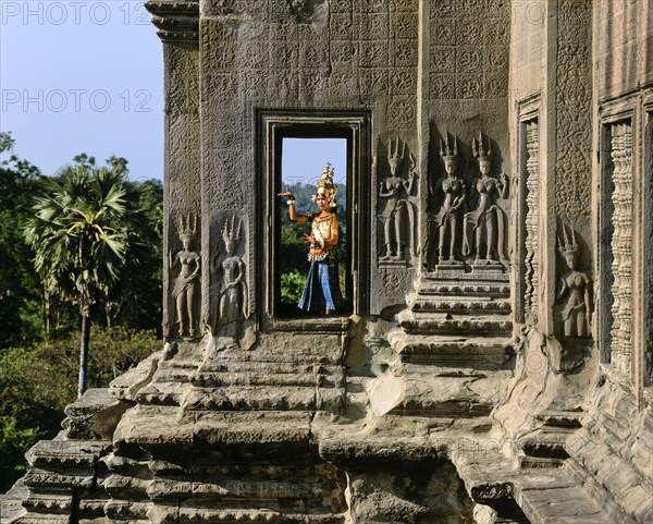 Temple dancer or apsara in a window of the temple of Angkor Wat beside apsara reliefs