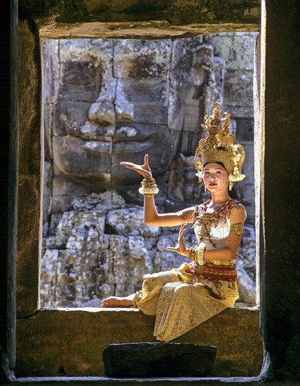 Temple dancer or apsara sitting in a window in front of a face tower at Bayon Temple