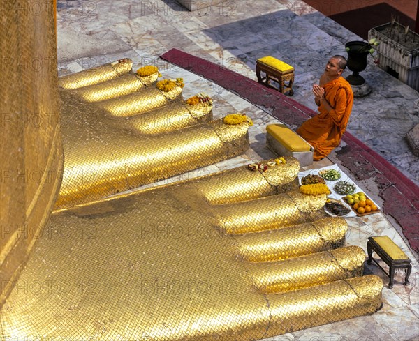 Monk praying at the feet of the golden Buddha statue of Wat Intharawihan