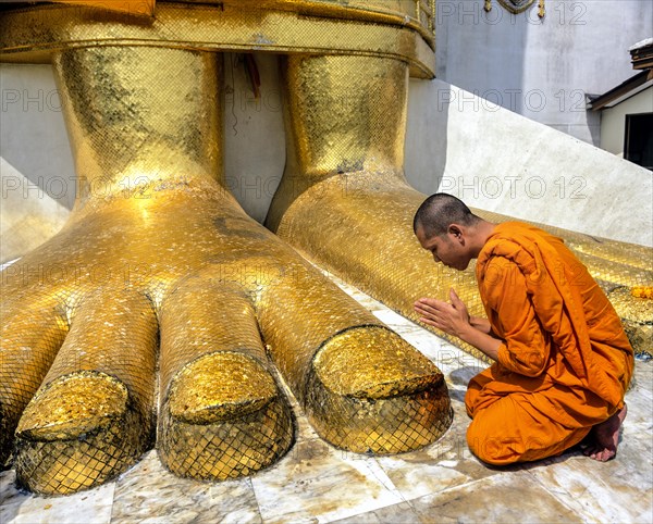 Monk praying at the feet of the golden Buddha statue of Wat Intharawihan