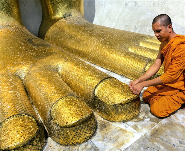 Monk praying at the feet of the golden Buddha statue of Wat Intharawihan