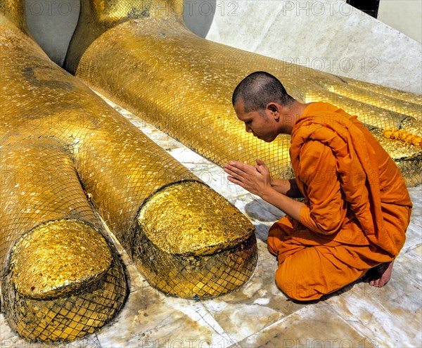 Monk praying at the feet of the golden Buddha statue of Wat Intharawihan