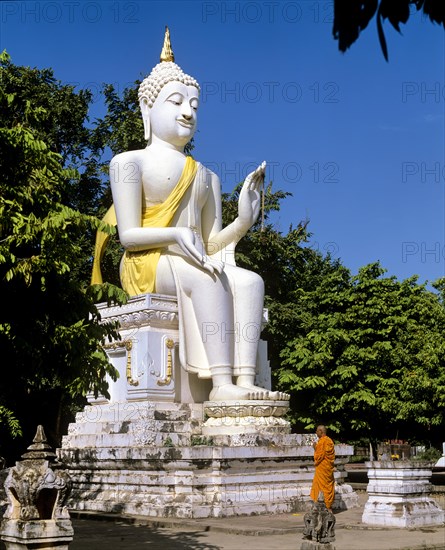 Monk standing in front of a white seated Buddha statue at Wat Mahathat