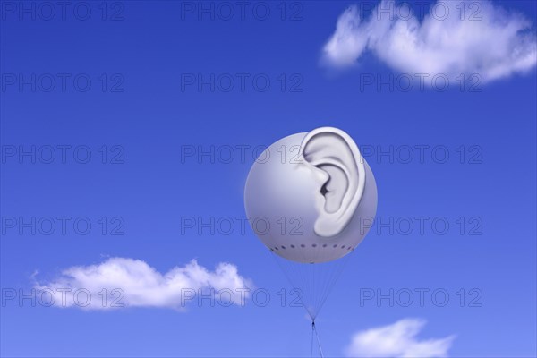 Tethered balloon with a three-dimensional human ear against a blue sky with white clouds