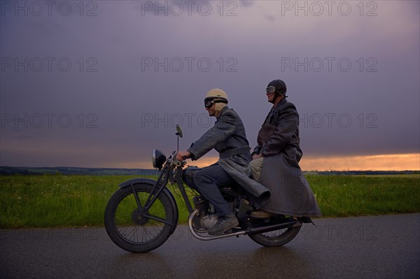 Two vintage motorcyclists in front of a dramatic cloudy sky